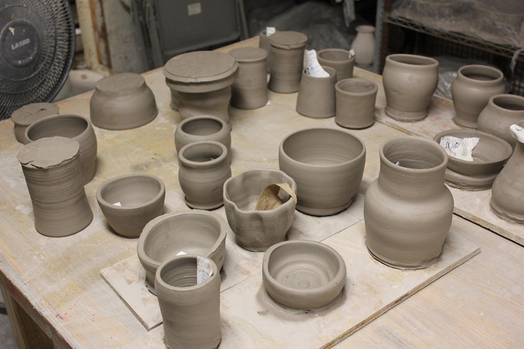 Multiple clay vessels (vases, bowls, cups) sitting on a table in a ceramics studio